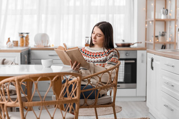 Sticker - Young woman reading book at dining table in kitchen