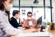 © Art_Photo - Asian business man and woman using laptop computer working and planning meeting in quarantine for coronavirus wearing protective mask with social distancing while sitting on office desk