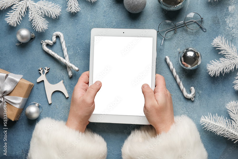 Santa Claus with tablet computer and Christmas decor on blue background