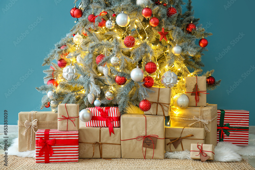 Gifts under glowing Christmas tree near blue wall