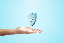 Close Up Of Female Hand Holding Creative Antivirus Shield Icon On Light Blue Background. Secure Phone Usage, Protection And Web Safety Concept.
