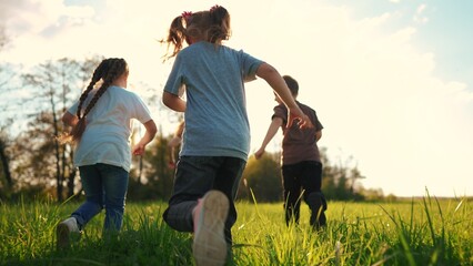 kids run in the park. a large group of a team of children running back view sunlight in the summer on the grass in the park camera movement. people in the park happy family kid lifestyle dream concept