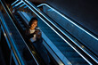 © Drobot Dean - Young asian woman using mobile phone while standing on escalator indoors
