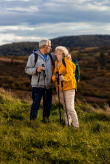 active senior couple with backpacks hiking together in nature on autumn day.