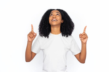 Wall Mural - Happy multiracial woman pointing up at ads. Excited young female model with dark curly hair in white T-shirt looking up, smiling and laughing, showing two options with fingers. Advertisement concept