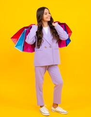 Poster - Beautiful fashion teenager child girl with shopping bags on yellow background. Shopaholic shopping and fashion. Kid with shopping sale bags.