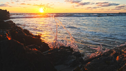 Poster - Beautiful natural landscape with sandy beach  with big stones during sunset.  Sun over horizon and Rolling ocean waves to the rocky shore while sunset.  Summer tourist destination in Portugal. Travel