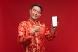Young asian man wearing Chinese red dress show smartphone with empty screen on red background for Chinese new year festival
