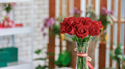 Closeup studio shot fresh red and pink petal roses bunch bouquet in glass vase placed on workshop table with other colorful flowers material for florist decorating arranging in floral store.