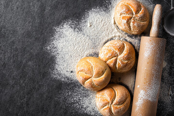 Poster - Mini bun bread on a dark stone background with rolling pin top view copy space. Home baking concept