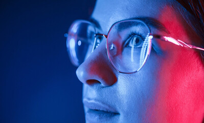 Wall Mural - In glasses. Close up view. Young beautiful woman is indoors in the studio illuminated by neon light