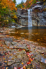 Wall Mural - Large waterfall over cliff edge into body of water with rocks and fall leaves
