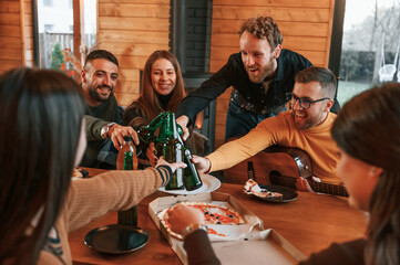 Wall Mural - With pizza and beer. Group of friends is having good weekend indoors in the wooden building together