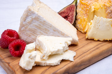 Board with french soft cheeses, Delice de Bourgogne French cow's milk cheese from Burgundy region of France and yellow langres cheese served with fresh raspberries