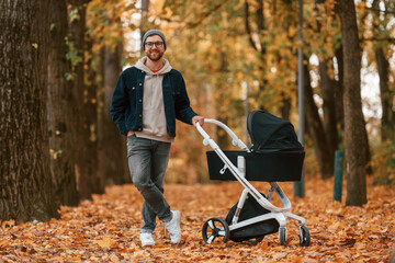 Wall Mural - Standing and enjoying a nature. Man with pram is having a walk in the autumn park