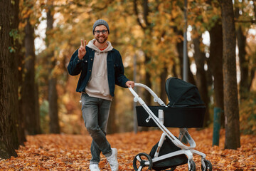 Wall Mural - Front view. Man with pram is having a walk in the autumn park