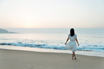 Wall Mural - Young asian woman relaxing on the beach at sunrise.