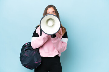 Wall Mural - Young sport woman with sport bag isolated on blue background shouting through a megaphone