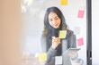 © David - Business female employee with many conflicting priorities arranging sticky notes commenting and brainstorming on work priorities colleague in a modern office.
