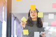 © David - Business female employee with many conflicting priorities arranging sticky notes commenting and brainstorming on work priorities colleague in a modern office.