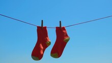 Pair Of Orange Socks Closeup Drying After Washing On Rope, Swaying In The Wind. Socks Hang On Rope With Clothespins Against The Blue Sky. Selective Focus.