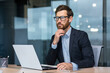 © Liubomir - Portrait of a young serious male businessman in the office at the table in headphones and with a laptop. Looks to the side.