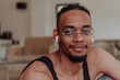 © .shock - Head shot of African American man wearing glasses and headphones sitting on living room floor