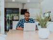 © .shock - African American man in glasses sitting at a table in a modern living room, using a laptop for business video chat, conversation with friends and entertainment