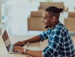 © .shock - African American man in glasses sitting at a table in a modern living room, using a laptop for business video chat, conversation with friends and entertainment