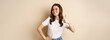 © Mix and Match Studio - Portrait of modern young woman showing thumbs up, like and approve, smiling pleased, recommending company or website, standing over beige background