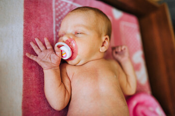 Wall Mural - A beautiful newborn baby, a little girl lies, sleeps in bed, with a pacifier in her mouth, eating on a blanket. Photography, childhood.