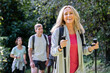 © PhotoAlto - Blonde middle aged lady carrying backback and hiking poles hiking in the woods with group of friends