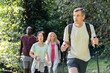 © PhotoAlto - Middle-aged man carrying backpack and hiking poles while hiking in the woods with diverse group of friends