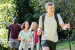 © PhotoAlto - Middle-aged man carrying backpack and hiking poles while hiking in the woods with diverse group of friends