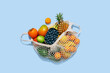 Shopping net bag with different exotic fruit top view on blue background. Pineapple passion fruit mango avocado lime grapes coconut. Blueberries. Grocery store supermarket delivery