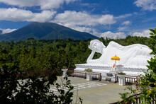 White Sleeping Buddha Statue In A Reclining Pose With A Mountain And Trees In The Background, Vihara Dharma Giri Temple; Tabanan, Bali, Indonesia