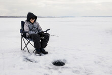 Boy Patiently Waiting For A Bite While Ice Fishing At Wabamun Lake; Wabamun, Alberta, Canada