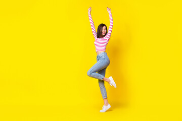 Wall Mural - Full size photo of nice gorgeous cheerful girl dressed striped shirt jeans white sneakers fists up isolated on yellow color background