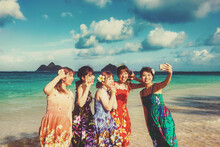 Group Of Young, Japanese Women On Vacation, Standing On The Beach In Floral Print Sundresses And Taking A Selfie Together; Lanikai Beach, Oahu, Hawaii, United States Of America