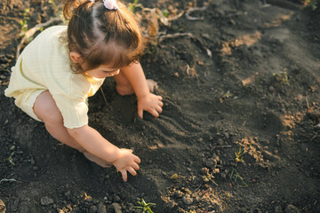 Portrait of a little baby girl pressing the soil with her hands. Summer vacation fun. Agriculture concept. Happiness concept.