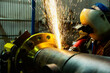 © Designpics - A welder wearing mask and eye protection is grinding a flange butt weld in a fabrication plant; Innisfail, Alberta, Canada