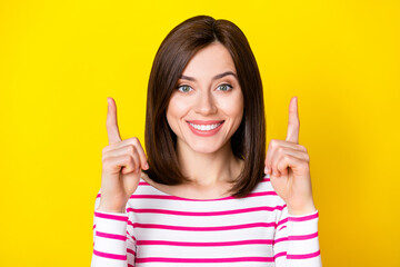 Wall Mural - closeup photo of young beautiful girl directing fingers up good news isolated on yellow color backgr
