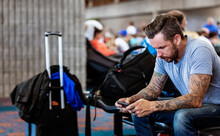 A man sits in an airport waiting area using his smart phone; Kahului, Maui, Hawaii, United States of America