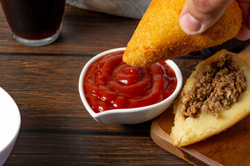 Wall Mural - dipping coxinha on the ketchup sauce. traditional brazilian fried coxinha snack fast food