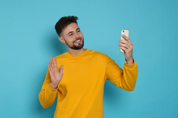 Wall Mural - Handsome man in yellow sweatshirt with phone on light blue background