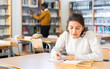 © JackF - Interested young Latina spending time in library, reading books and making notes. Self-education concept