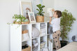 Little cute boy is watering indoor plants from a stylish watering can in a designer home interior.