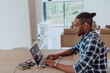 © .shock - African American man in glasses sitting at a table in a modern living room, using a laptop for business video chat, conversation with friends and entertainment