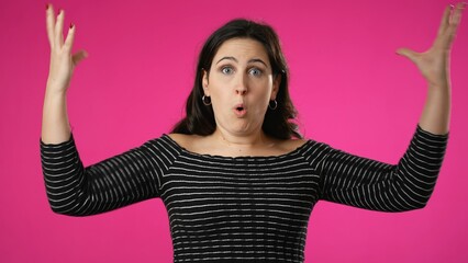 Pretty thinking young woman 20s, looks at camera gives mind blown gesture showing explosion of ideas posing on pink background.