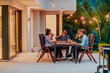© .shock - A group of young diverse people having dinner on the terrace of a modern house in the evening. Fun for friends and family. Celebration of holidays, weddings with barbecue.